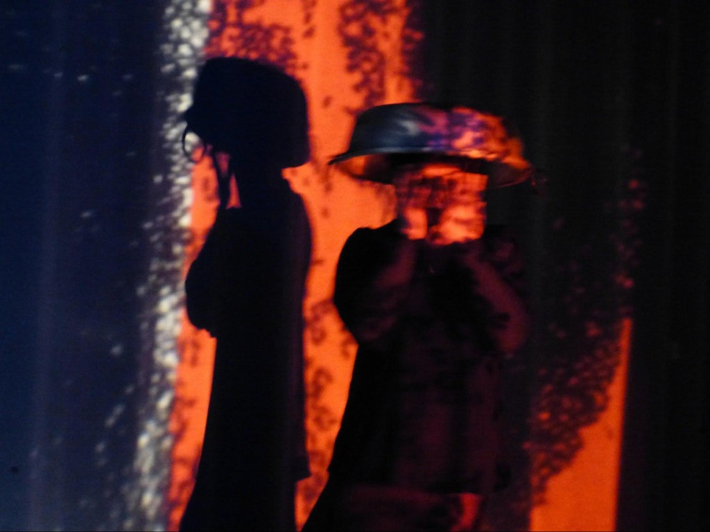 Two silhouettes against an orange-red wall — performance